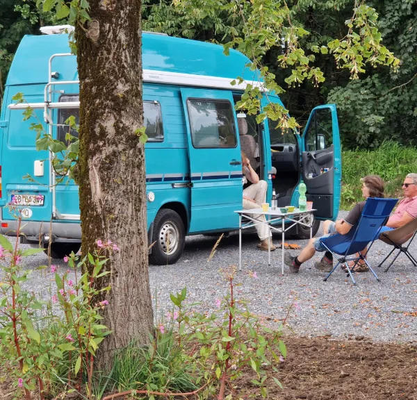 Camper sitzen entspannt neben ihrem türkisen Kastenwagen im Grünen